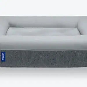 The Bowser Bed with a gray plush cushion and a darker gray fabric outer layer, displayed on a white background. The dog bed has a minimalistic design and features a small blue brand tag.