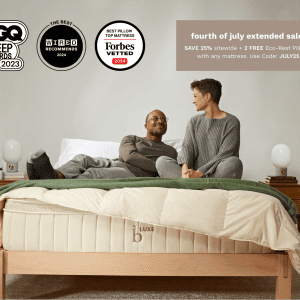 A man and a woman sitting on a bed covered with beige and green bedding. The wall above has award logos and a promotion reading, "Fourth of July extended sale! SAVE 25% sitewide + 2 FREE Eco-Rest Pillows with any Birch Luxe Natural Mattress. Use Code: JULY25.