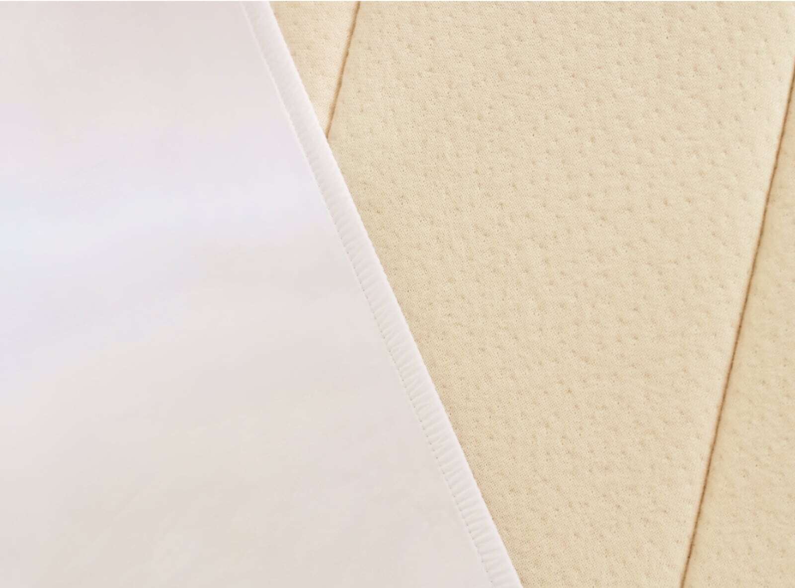 Close-up of two textures. The left side features a smooth, white sheet with a faint fold line, reminiscent of the Birch Natural Mattress, while the right side showcases a piece of beige, textured leather or faux leather with subtle diagonal stitching lines.