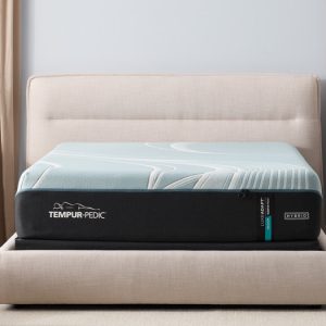 A neatly made bed showcases a Tempur-Pedic TEMPUR-LuxeAdapt® 13" Medium Hybrid Mattress with distinctive stitching and a sleek design. The bed frame is upholstered in light beige fabric, and two black nightstands with minimalist decorations sit on either side in a softly lit bedroom.