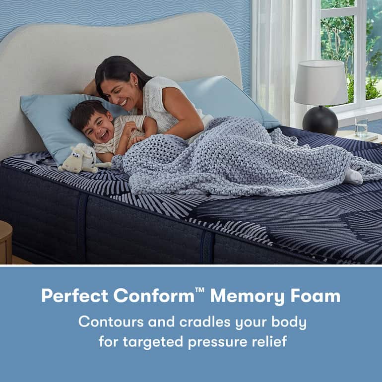 A woman and a child are lying on a bed together under a gray knit blanket. The child is smiling while cuddling a stuffed animal. The bed, featuring the Serta Perfect Sleeper X Mattress: Prescott Medium Firm, boasts body-conforming and pressure-relieving properties in the caption below.