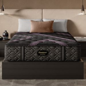 A modern bedroom showcasing a dark quilted Beautyrest Black® Series Three 15.25" Medium Mattress on a wooden bed frame, flanked by two matching nightstands with hanging pendant lights above. The bed has beige and brown pillows, and there are books and decorative items on the nightstands.