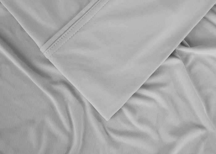 A close-up of light gray fabric from a Hyper-Cotton Sheet Set (Copy), showcasing its smooth, soft texture. One part of the sheet is neatly folded, revealing detailed stitching, while the remaining portion is gently wrinkled and spread out.