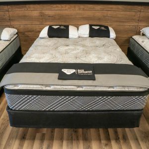 A showroom showcasing three Spring Air 300 Hybrid mattresses on solid wooden flooring. The central mattress, light gray with a "Back Supporter" label, is flanked by two other identical models. Each bed is styled with pillows and a matching color scheme that complements the wood-paneled wall.