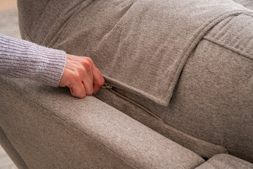 A person’s hand is unzipping a pocket on the back of a light gray upholstered Model 2 Plus Shell Exclusive sofa.