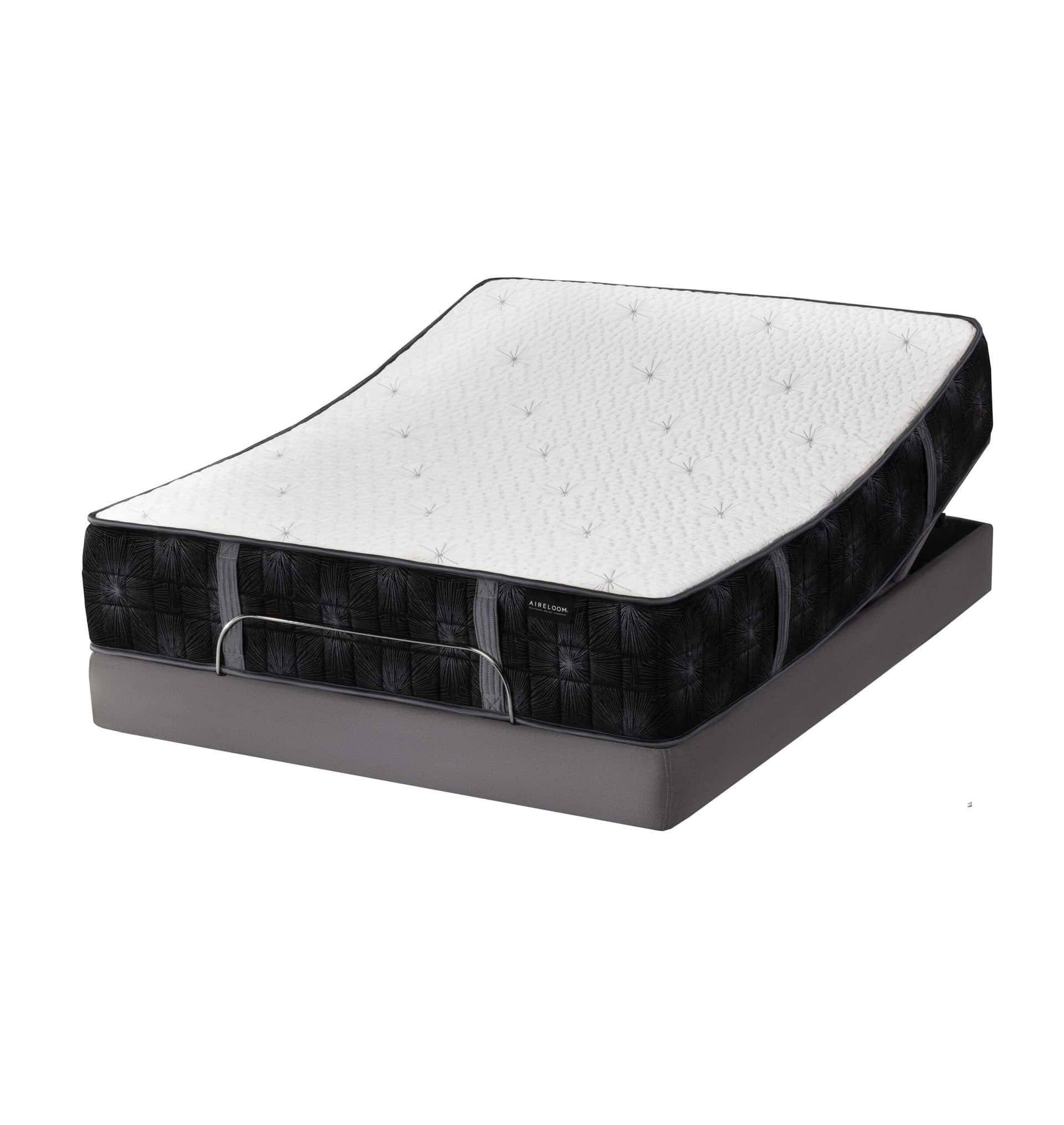 The Summit Luxury Firm mattress, featuring a white quilted top and black textured sides, is displayed on an adjustable gray bed base with the head section elevated for enhanced support.