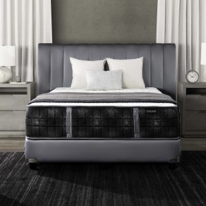 A modern bedroom with a gray upholstered bed frame, a Summit Luxury Firm mattress with black pattern, white bedding, two nightstands with lamps, a clock, and white curtains against a gray wall.