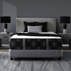 A modern bedroom with a gray Summit Plush (Copy) upholstered bed, black and white bedding, two black table lamps on matching gray nightstands, and a gray patterned rug on wood flooring.