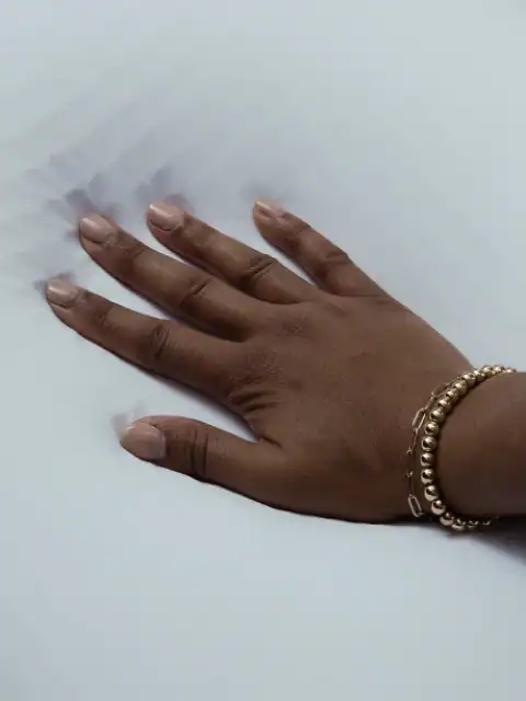 A hand with a gold bracelet presses into the soft, white surface of the Purple Free-Form Pillow, creating an indentation.