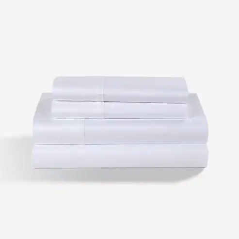 A neatly folded stack of crisp white Hyper - Cotton Performance Sheets, including pillowcases and a fitted sheet, displayed on a plain light background.