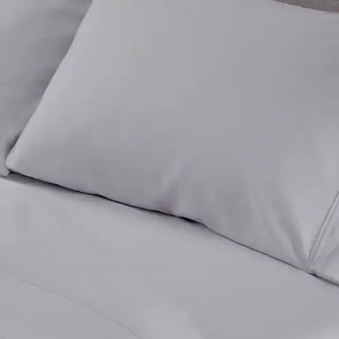 A close-up of a white pillow and Hyper - Cotton Performance Sheets neatly arranged on a bed, creating a clean and comfortable look.