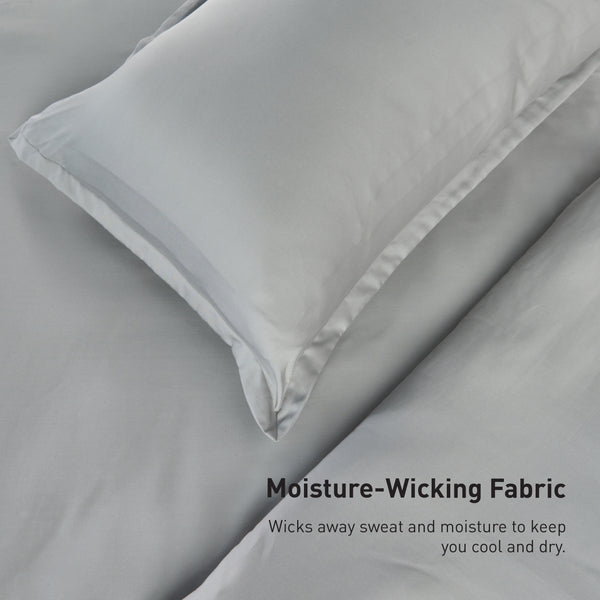 A close-up of a bed with light gray bedding from our Performance Duvet & Sham Set - Solid. Text reads: "Moisture-Wicking Fabric. Wicks away sweat and moisture to keep you cool and dry.