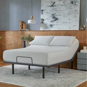 A modern bedroom features the Baselogic™ Silver Adjustable Base in an elevated position with white bedding and pillows, set against wood paneling, a grey accent wall, abstract artwork, pendant lights, and minimal décor.