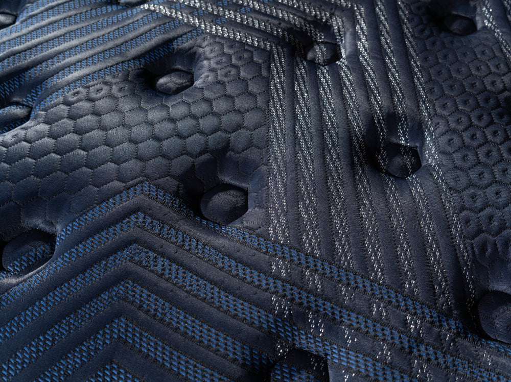 Close-up of ThermoBalance Soft’s dark blue, patterned surface with hexagonal and linear stitching, indented circular details, and varied textures highlight its soft mattress feel.
